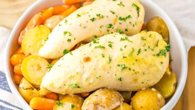 A bowl with two cooked chicken breasts garnished with herbs, served over baby potatoes and carrots.