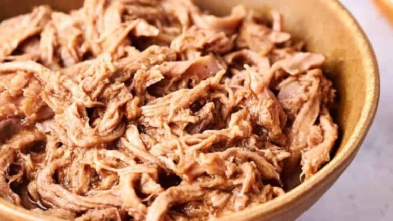 A bowl of shredded cooked meat sits on a light-colored surface.