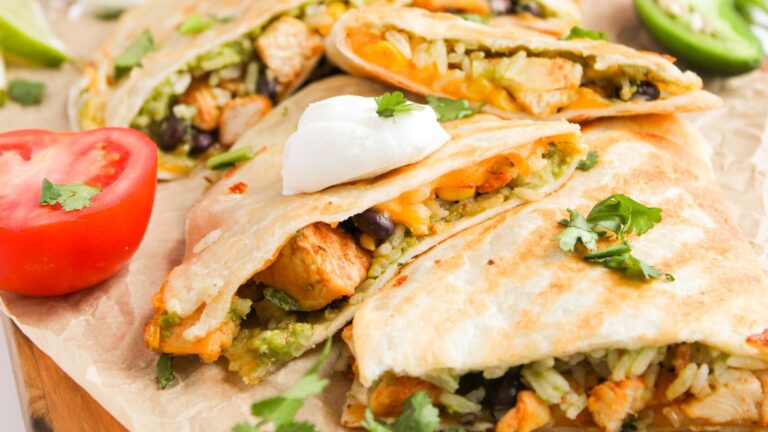 Quesadillas filled with rice, beans, and chicken, topped with sour cream and cilantro. Sliced tomato and jalapeño are on the side.