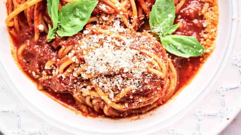 Plate of spaghetti topped with tomato sauce, grated cheese, and basil leaves.