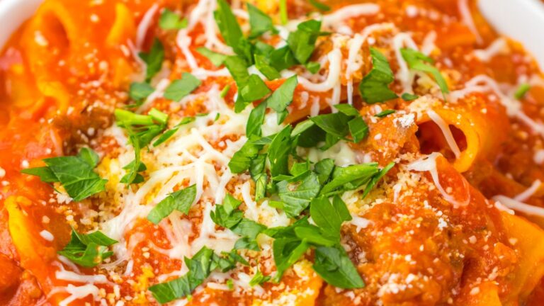A close-up of pasta in red sauce, topped with grated cheese and chopped parsley.