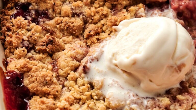 Close-up of a fruit crumble dessert topped with a scoop of vanilla ice cream.