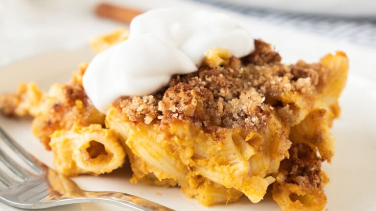 A serving of creamy pasta bake topped with a crumbly brown crust and a dollop of white sauce, on a plate.