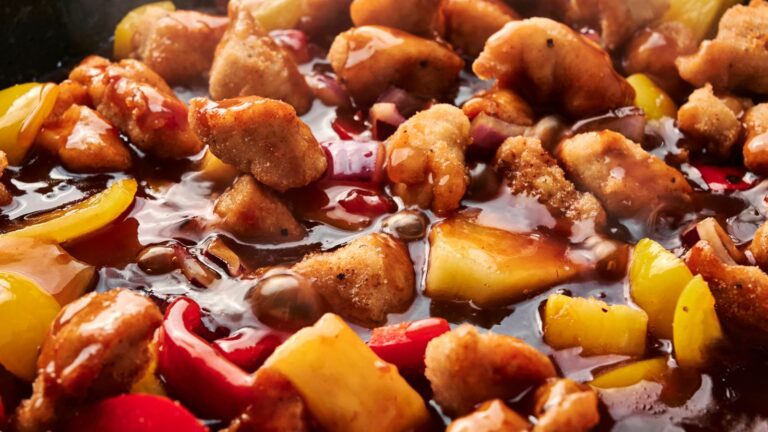 Close-up of sweet and sour chicken with bell peppers and pineapple chunks in sauce.