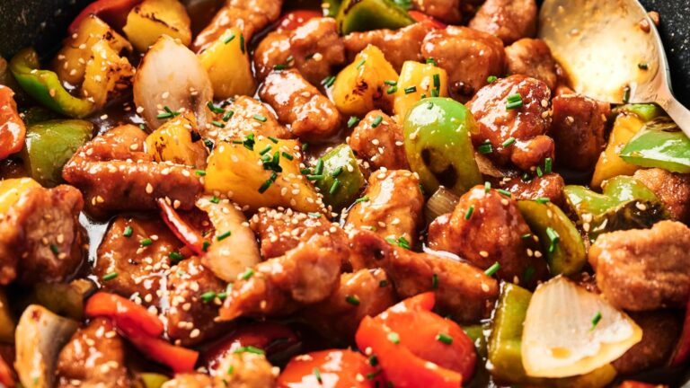 A dish of sweet and sour pork with pineapple, bell peppers, and onions garnished with sesame seeds.