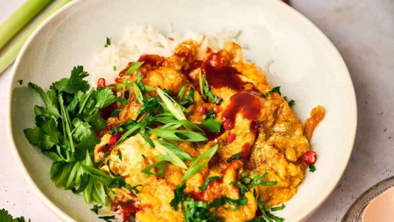 A plate of rice topped with scrambled eggs, sliced green onions, and a red sauce. Garnished with cilantro.