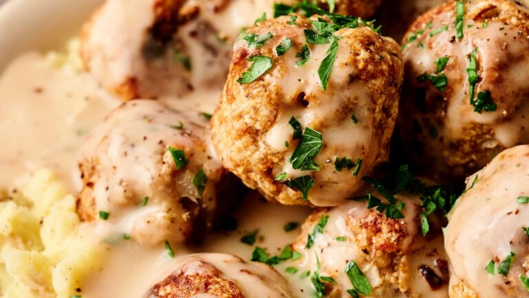 Meatballs with creamy sauce, garnished with chopped parsley, served over mashed potatoes.