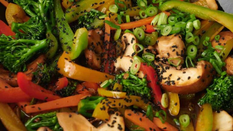 A colorful vegetable stir-fry with bell peppers, broccoli, mushrooms, and green onions, sprinkled with black sesame seeds.