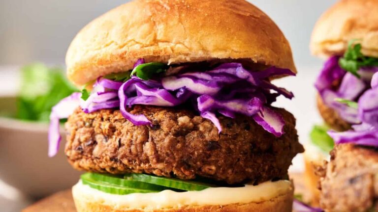 A burger with a patty, purple cabbage, cucumbers, and sauce, served in a bun.