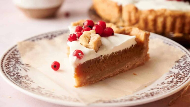Slice of pie topped with whipped cream and red berries on a decorative plate.