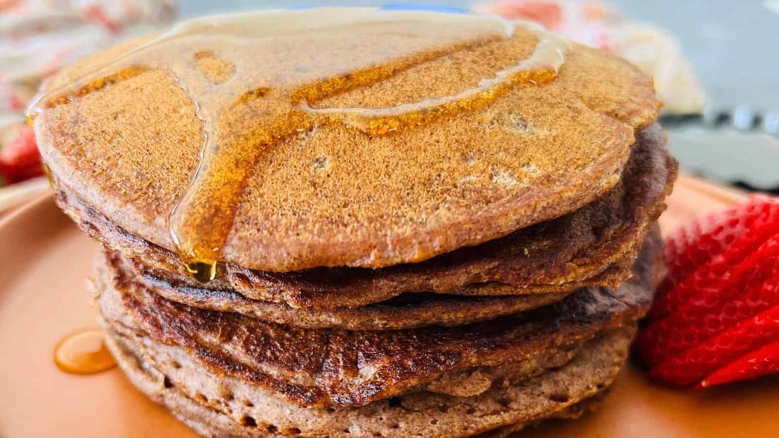 Stack of Ragi pancakes with syrup drizzled on top, accompanied by strawberries on the side.