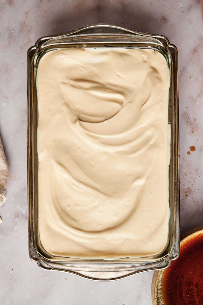 A glass baking dish filled with smooth, swirled tiramisu cream mixture rests elegantly on a marble surface.