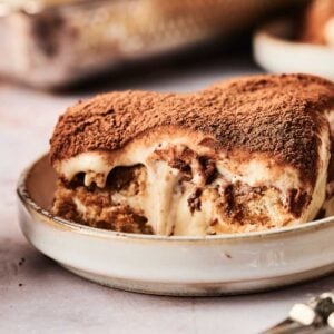 A generous slice of classic tiramisu rests on a small plate, its delicate layers visibly tempting with each glance and a fine dusting of rich cocoa powder gracing the top.
