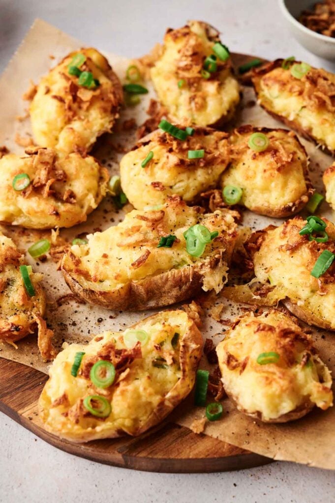 Twice baked potatoes topped with melted cheese, crispy onions, and green onions are served on a rustic wooden platter.