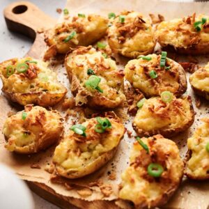 Twice-baked potatoes topped with cheese and green onions rest on a wooden board lined with parchment paper.
