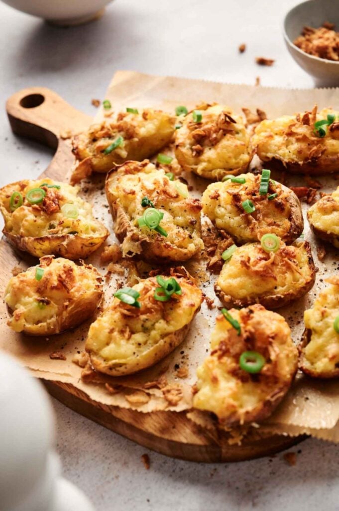 Twice-baked potatoes topped with cheese and green onions rest on a wooden board lined with parchment paper.