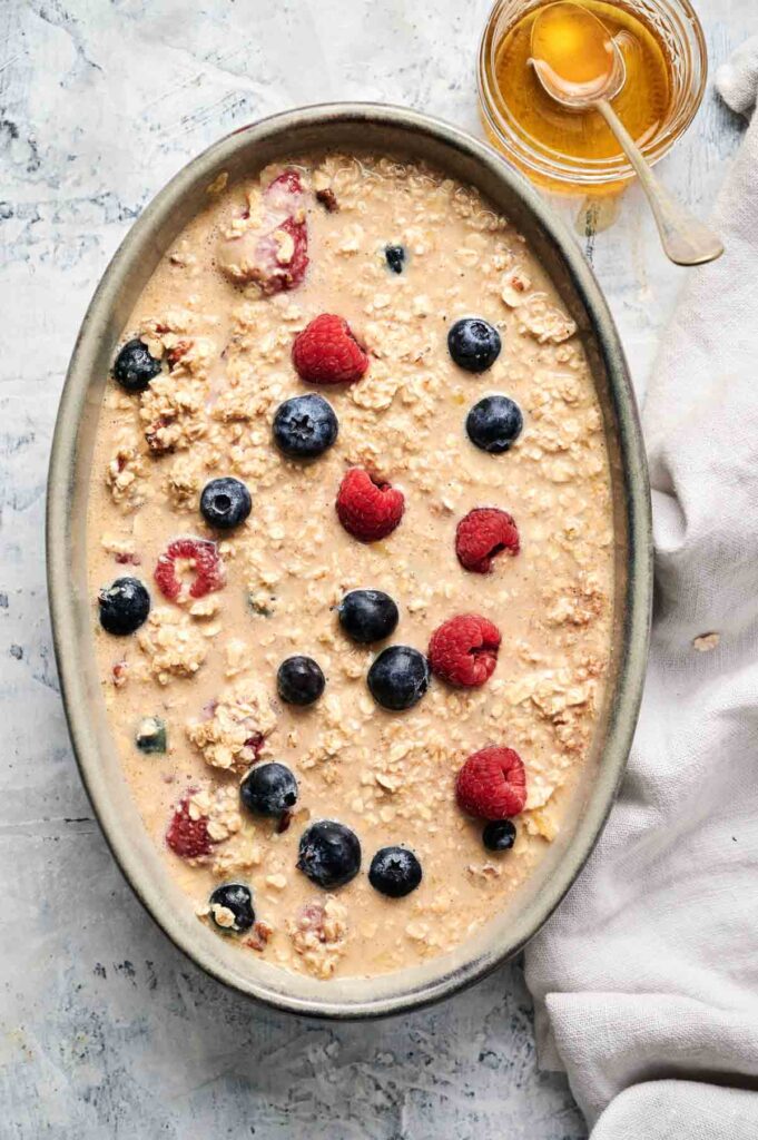 A bowl of oatmeal topped with raspberries and blueberries next to a jar of honey.