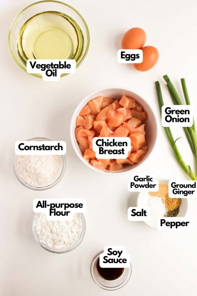 Ingredients for General Tso’s Chicken are laid out on a white surface: chicken breast, vegetable oil, eggs, green onion, cornstarch, all-purpose flour, soy sauce, garlic powder, ground ginger, salt, and pepper.