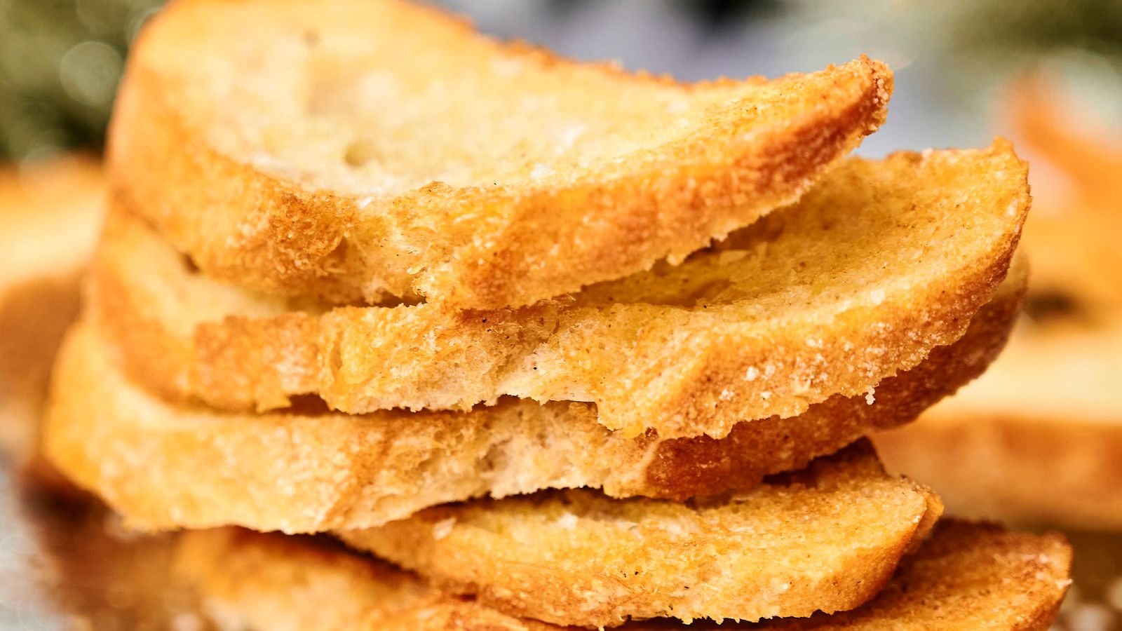 Slices of crispy toasted bread with a golden-brown crust, displayed in a pile.