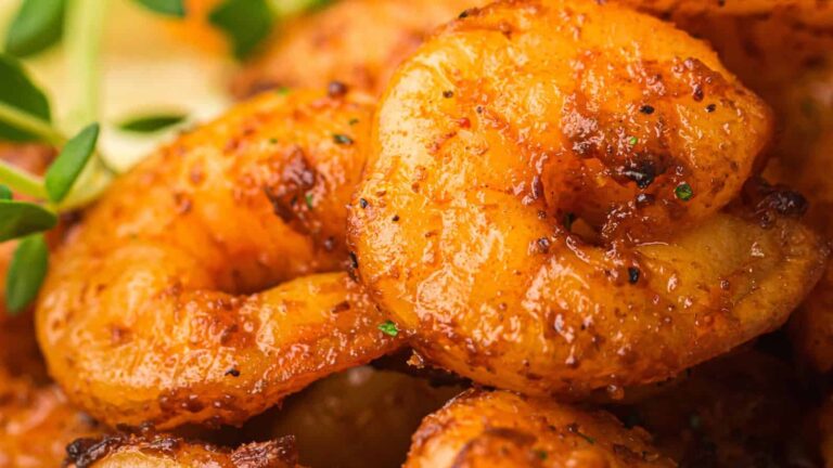 Close-up of seasoned, grilled shrimp with a golden-brown crust, garnished with fresh herbs.