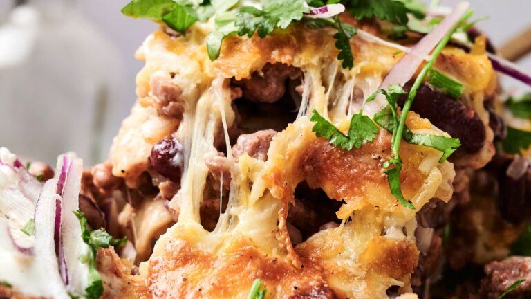 Close-up of cheesy nachos topped with melted cheese, beans, chopped red onions, and fresh cilantro.