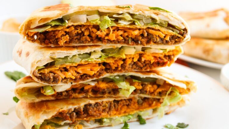 A close-up of tortilla wraps filled with ground meat, melted cheese, lettuce, and onions, stacked on a white plate.