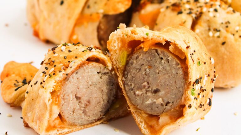 Sliced sausage rolled in a pastry dough topped with seeds, displayed on a white surface.