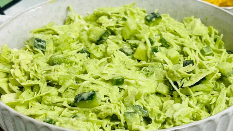 A white bowl filled with chopped cucumbers and shredded green vegetables, mixed in a creamy green dressing.