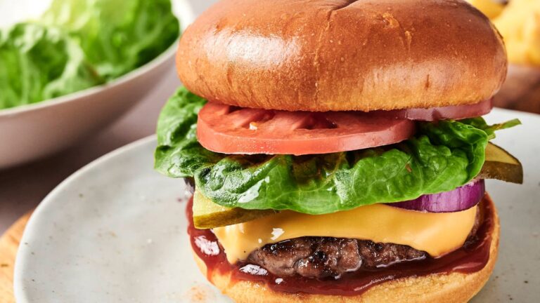 A cheeseburger with lettuce, tomato, pickles, and onion on a plate.