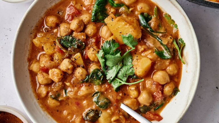 A bowl of chickpea curry with spinach, potatoes, tomatoes, and garnished with cilantro.