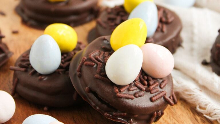 Chocolate-covered cookies topped with chocolate sprinkles and pastel-colored candy eggs on a wooden surface.