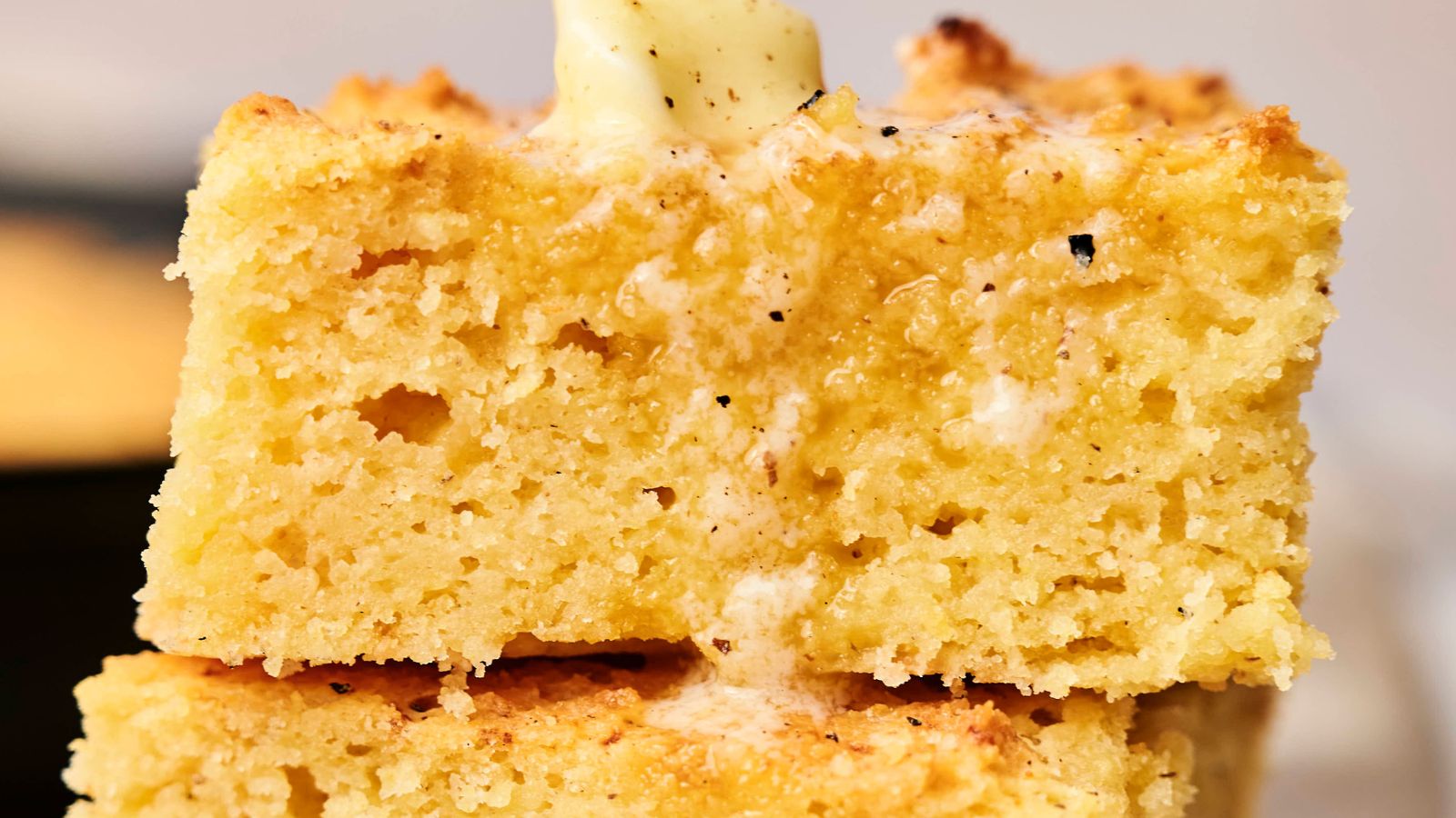 Close-up of two stacked pieces of cornbread with melted butter on top, showcasing a golden-brown crust and moist, crumbly texture.