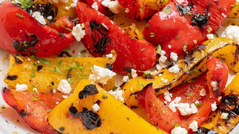 Grilled red and yellow bell peppers garnished with crumbled feta cheese and herbs.