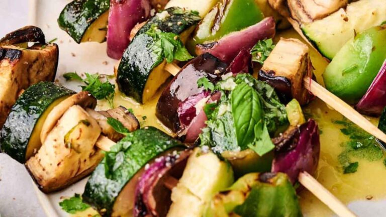 Close-up of vegetable skewers featuring zucchini, eggplant, red onion, and bell pepper with herbs, served on a platter.