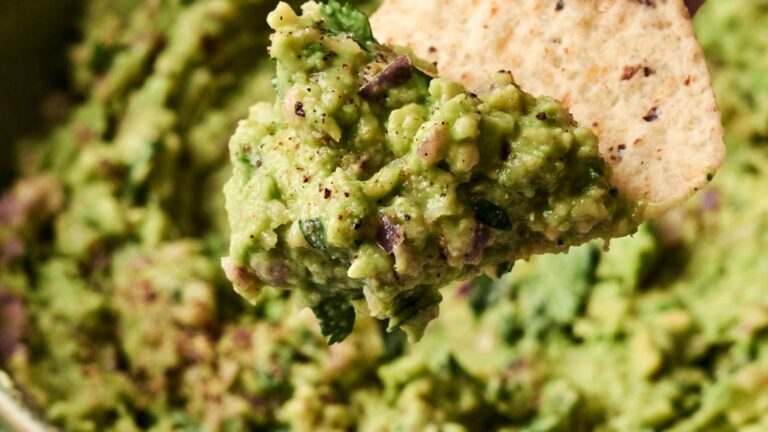Close-up of a tortilla chip dipped in guacamole, showcasing its creamy texture and herbs.