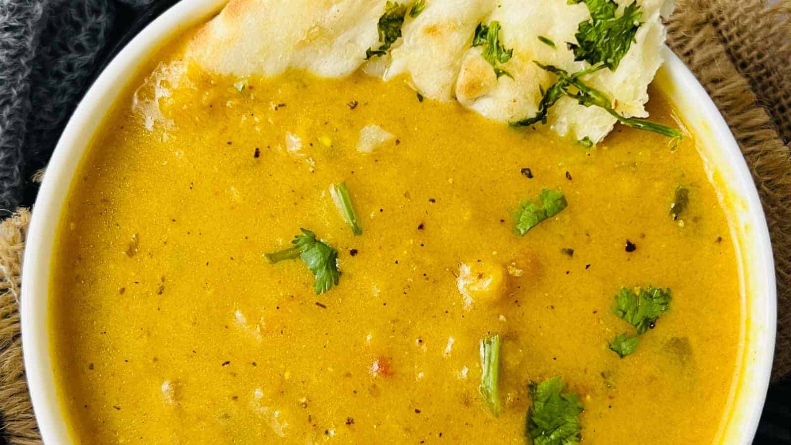A bowl of yellow curry soup garnished with herbs, served with a piece of flatbread.