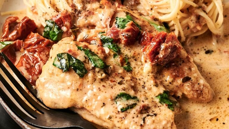 Chicken in creamy sauce with spinach and sun-dried tomatoes, served alongside spaghetti, with a fork on the side.