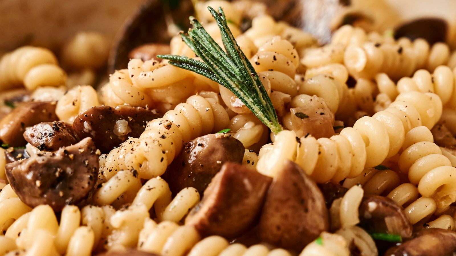 Close-up of fusilli pasta with mushrooms, garnished with rosemary and black pepper.