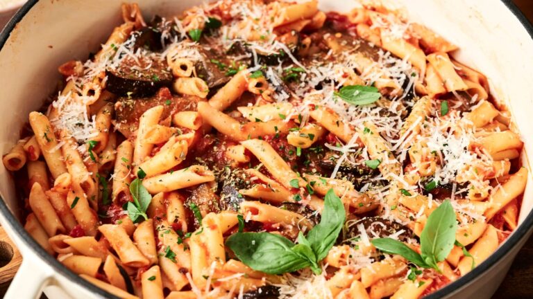 Pasta in a white dish with tomato sauce, grated cheese, and garnished with fresh basil leaves.