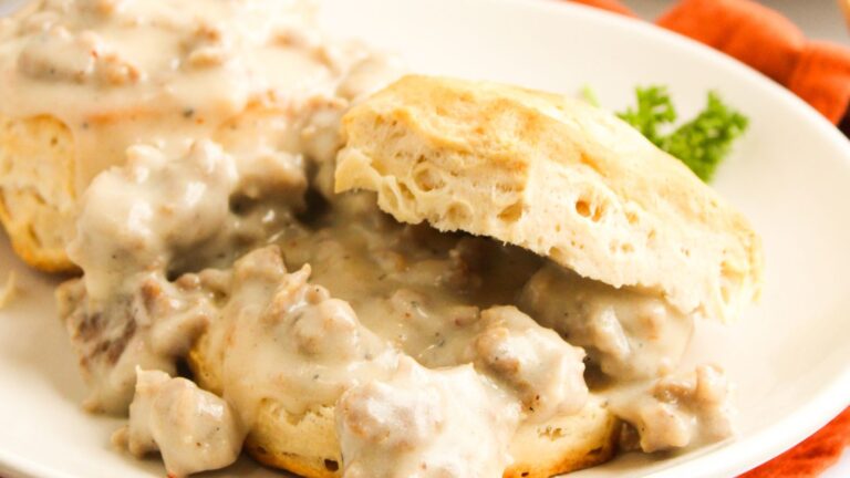 Biscuits topped with sausage gravy on a white plate, garnished with parsley.