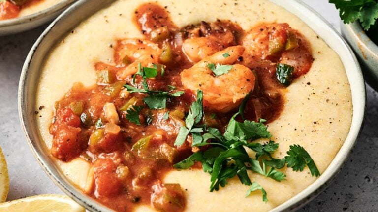 A bowl of creamy grits topped with shrimp in a tomato-based sauce and garnished with fresh parsley.