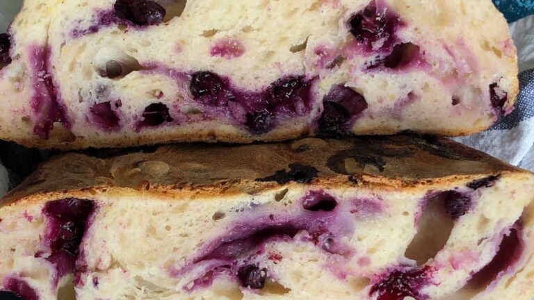 Close-up of a sliced bread loaf with swirls and chunks of purple berries baked into the dough.