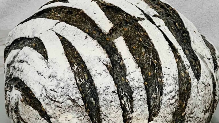 A round loaf of artisanal bread with a dark crust and white flour patterns on top.
