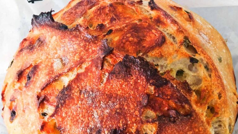 Close-up of a round, crusty golden-brown loaf of bread with a rough texture and darkened areas on the surface.