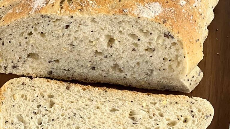 A loaf of seeded bread with a slice cut off, showing the textured interior with visible seeds.