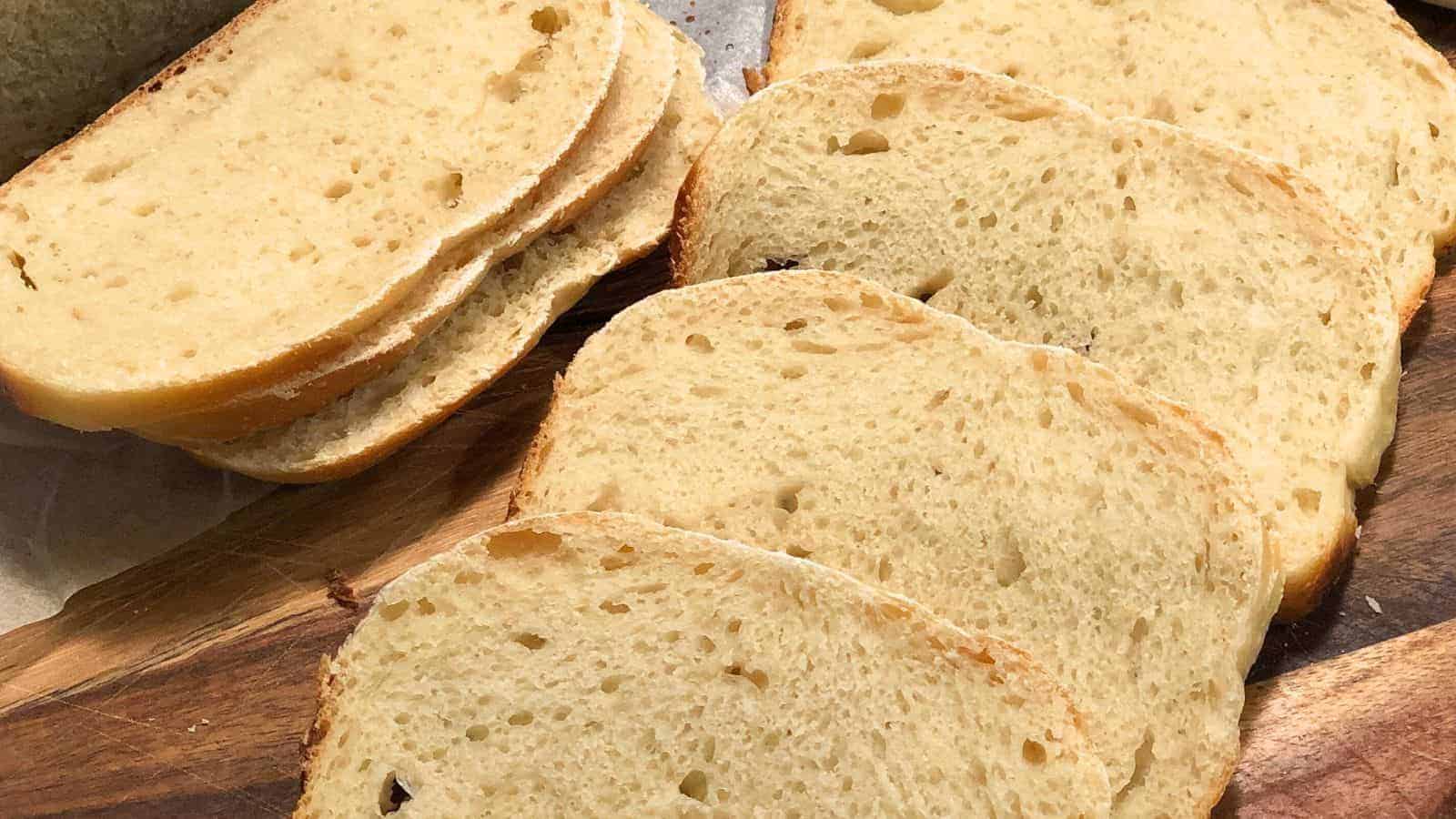 Seven slices of Sourdough Sandwich Bread arranged on a wooden cutting board.