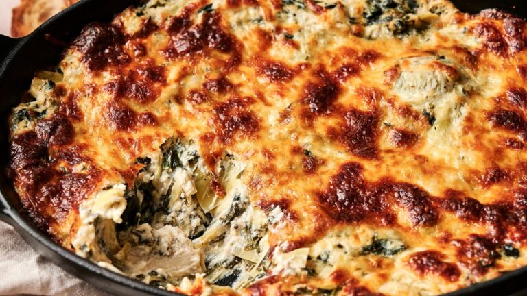 Baked spinach and artichoke dip in a skillet with golden, slightly charred cheese on top, and a portion scooped out.