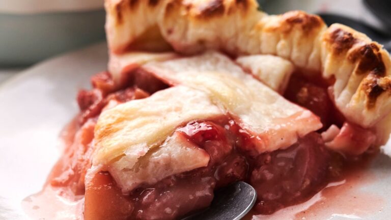 A slice of peach and berry pie with a golden brown crust and lattice design, served on a white plate.