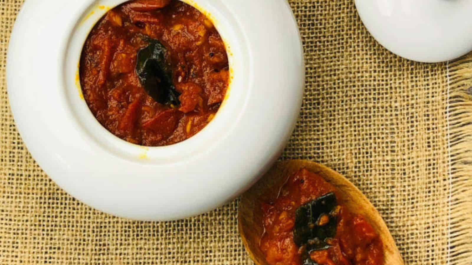 A white bowl filled with red curry and a wooden spoon with a small portion of the curry, placed on a burlap surface.