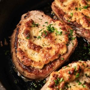 Sizzling in a skillet, these pork chops are crowned with a golden melted cheesy crust and garnished with fresh chopped herbs.